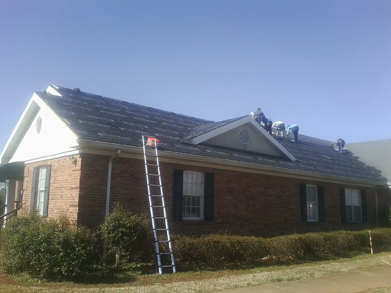 Crew tearing shingles off a brick ranch roof with a ladder set — Metal Roof Repair work by our crew in South Acworth
