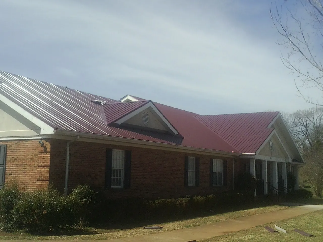 Red metal roof with gabled entries on a long brick building, from a Hail Damage Roof Repair job in South Acworth