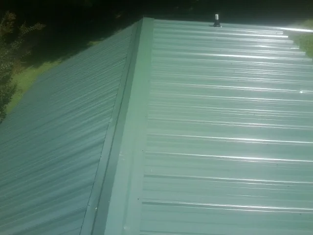 New green metal panels meeting at the ridge of a roof — Flat Roof Repair work by our crew in South Acworth