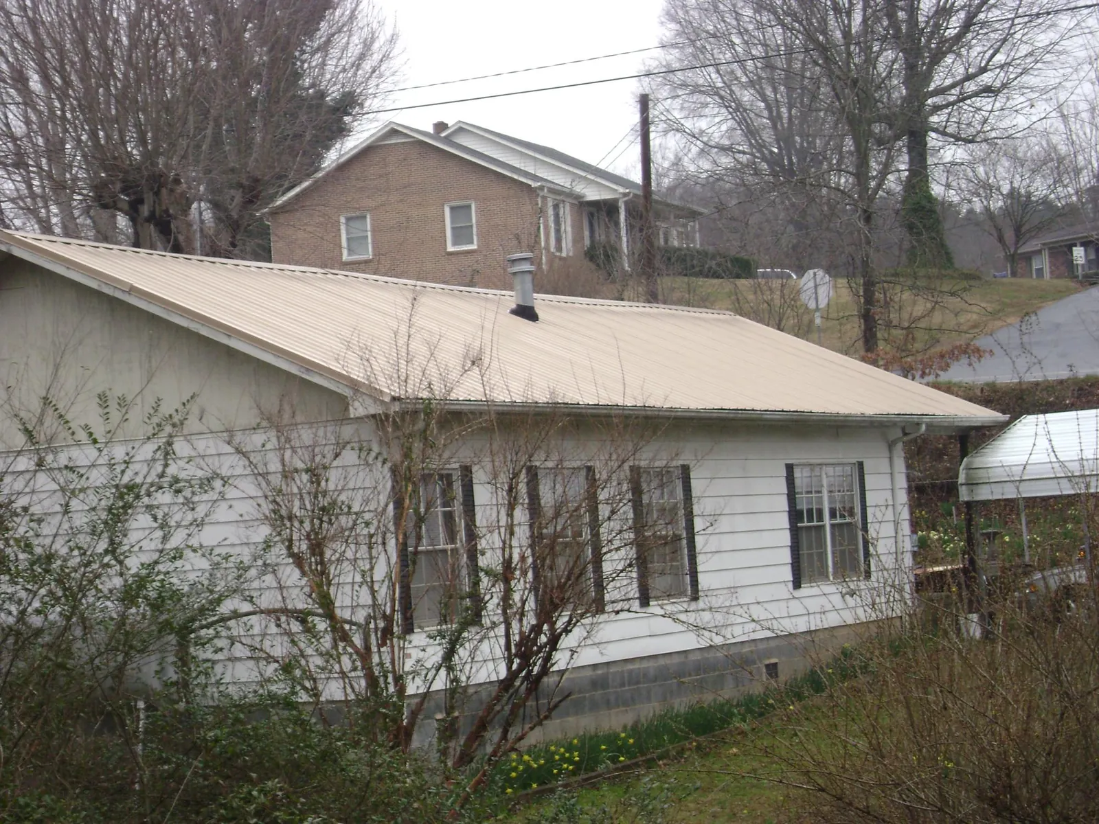 Tan metal roof on a white sided house set into a hillside — Commercial Roofing by Roofing Brothers in South Acworth